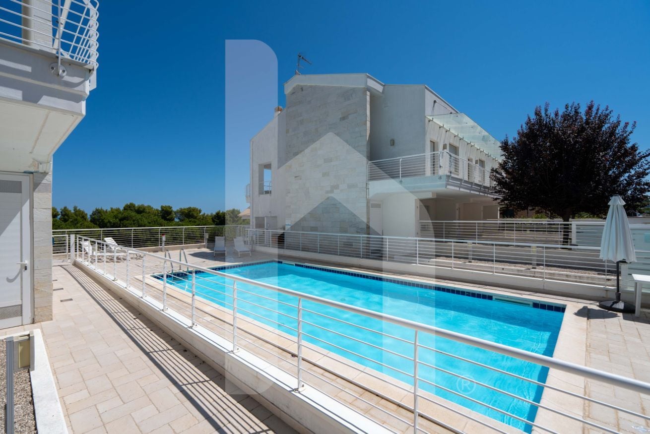 Una piscina con acqua cristallina circondata da una recinzione bianca e un edificio dal design moderno.