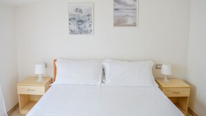 A bedroom with a bed, two bedside tables, and two wall-mounted paintings.