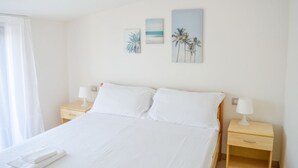 A hotel room with a bed, two nightstands, and wall art depicting palm trees and a beach scene. - G.Bay C25 - Second floor apartment with balcony and hill view (Foggetta)