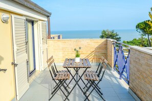 Un balcon avec une table et des chaises, une vue sur la mer et une porte bleue.