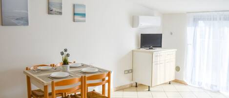 A dining area with a table set for four, a white cabinet with a television, and artwork on the wall.