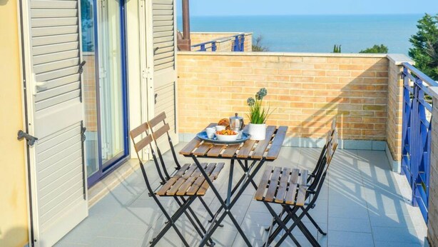 Ein Balkon mit Tisch für zwei Personen, einem Blumentopf und Blick aufs Meer.