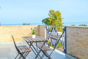 A balcony with a wooden table and chairs, a potted plant, and a view of the sea. - G.Bay C28 - Second floor apartment with balcony and hill view (Foggetta)