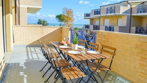 Un balcón con una mesa lista para comer, con vista a una zona residencial y al mar.