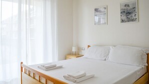 Una cama bien hecha con sábanas blancas, una mesita de noche con una lámpara y dos cuadros enmarcados en la pared.