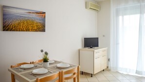 A dining area with a table set for two, a potted plant, and a painting of a landscape. - G.Bay D08 - Ground floor apartment with balcony and pool view (Foggetta)