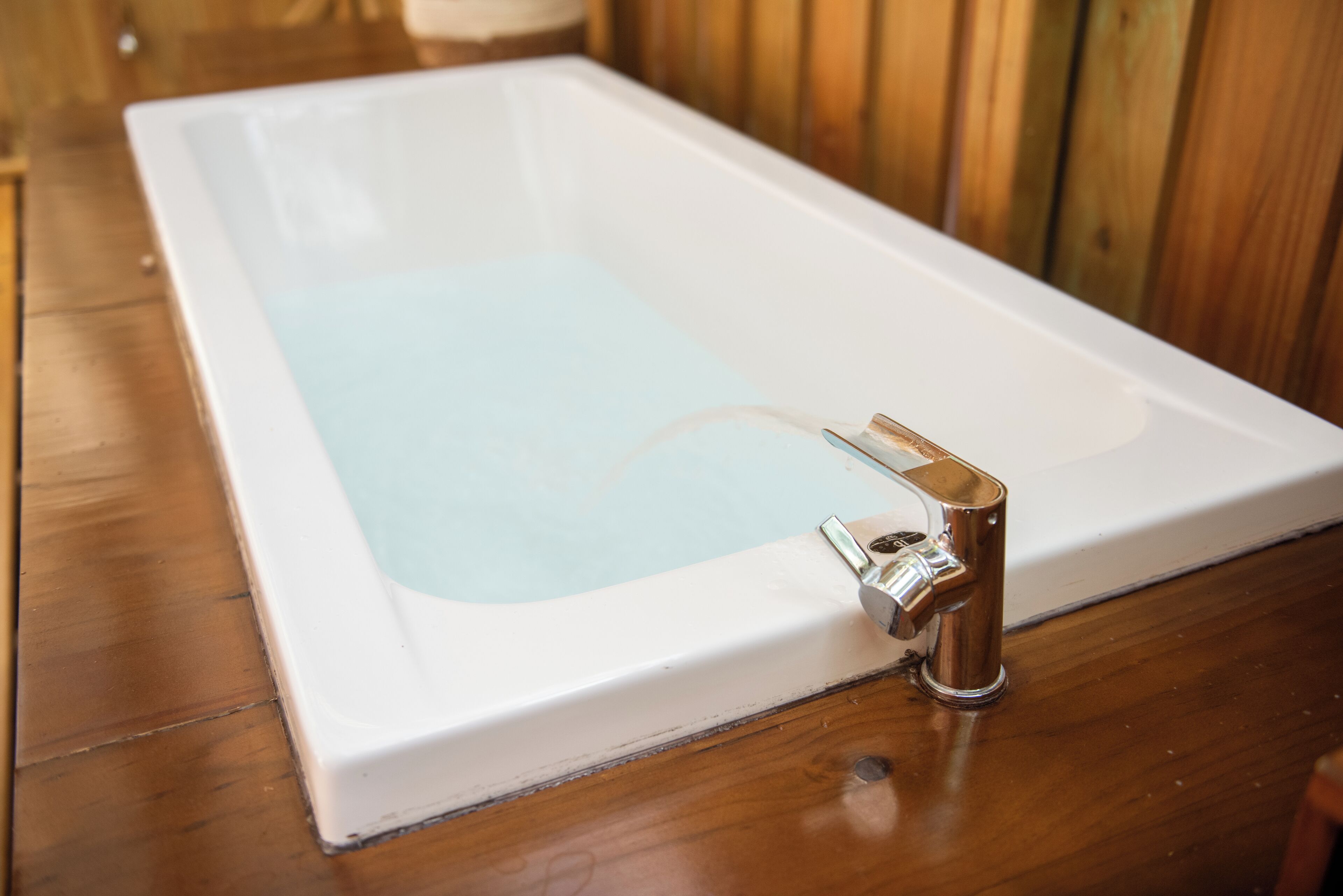 Una bañera rectangular con grifo de cromo sobre piso de madera.