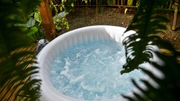 Un bain à remous dans un jardin agrémenté d’une terrasse en bois et de verdure.