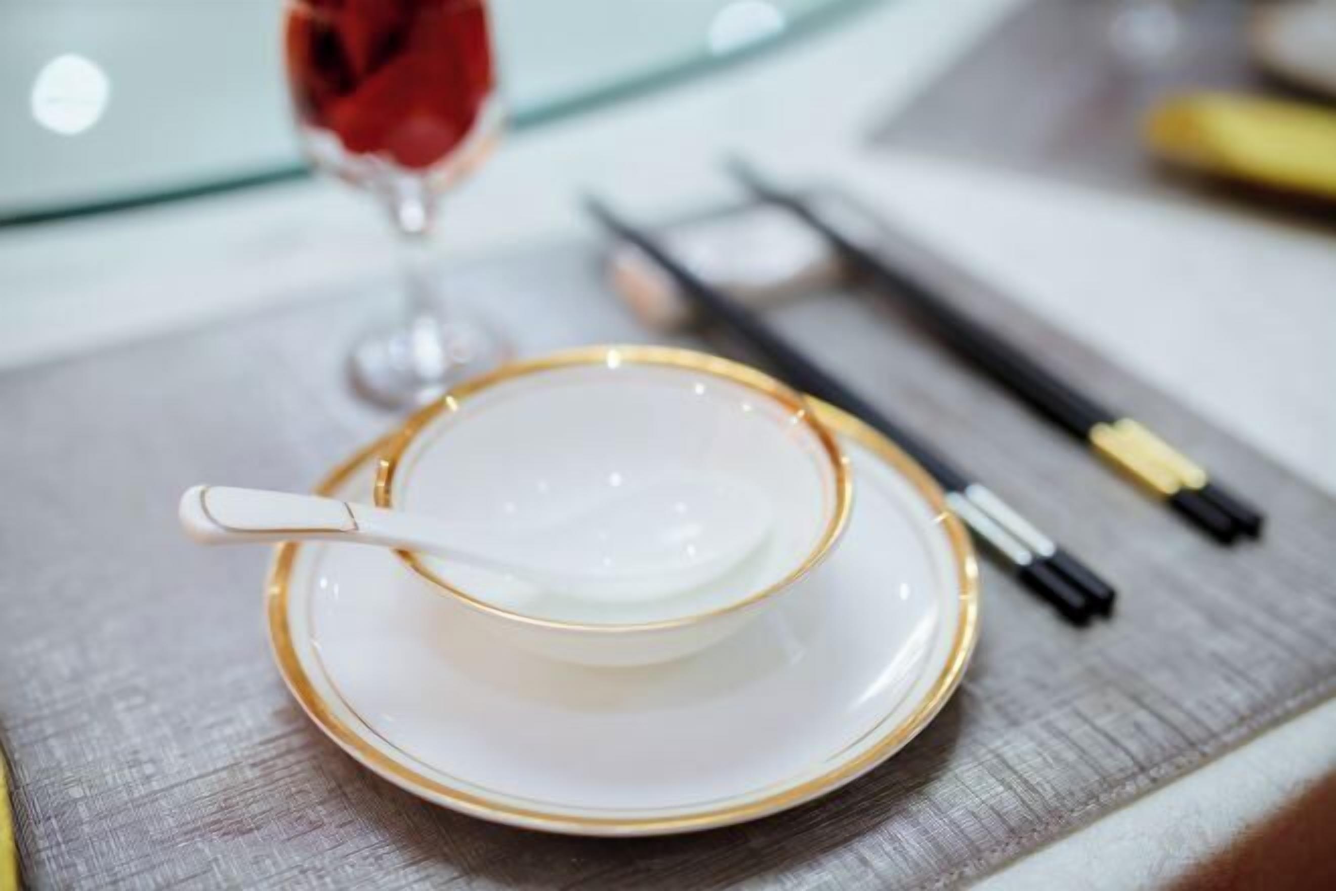 A white and gold teacup and saucer with a spoon on a wooden table.