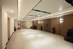 A hotel corridor with a wooden floor, a seating area, and a row of doors.
