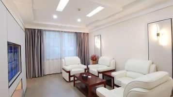 Una habitación de hotel moderna con sofás de cuero blanco, una mesa de centro de madera y un ventanal con cortinas.