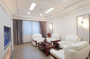 Una habitación de hotel moderna con sofás de cuero blanco, una mesa de centro de madera y un ventanal con cortinas.