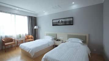 A hotel room with two beds, a desk, a chair, and a window with curtains.