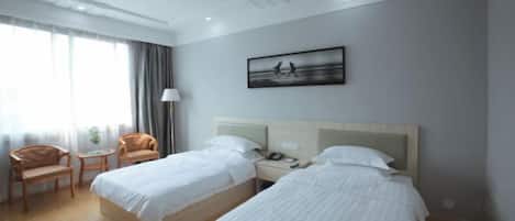 A hotel room with two beds, a desk, a chair, and a window with curtains.