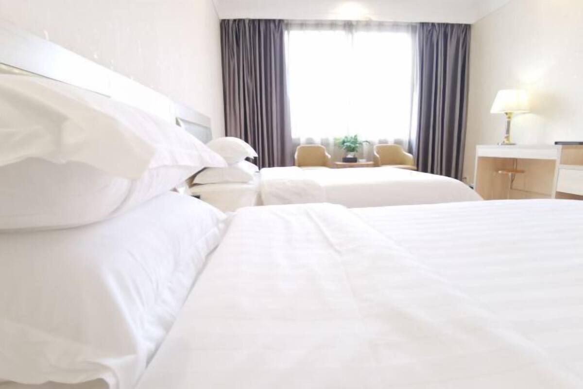 Ett hotellrum med två sängar, ett skrivbord, en stol och ett fönster med gardiner.
