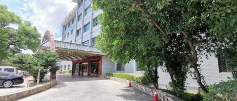 A hotel entrance with a covered walkway, a parking area, and a tree-lined pathway.