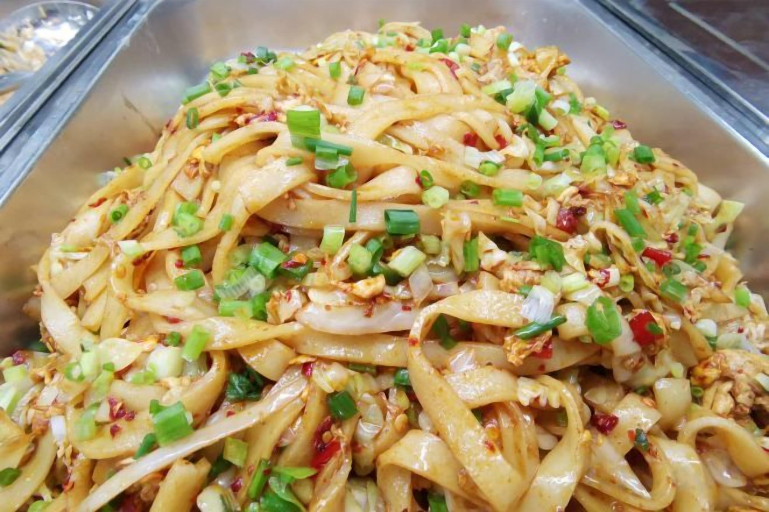 A stainless steel food serving tray with noodles and chopped green onions.