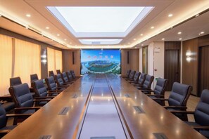 Une salle de conférence avec une longue table, des chaises, un grand écran et une lucarne.