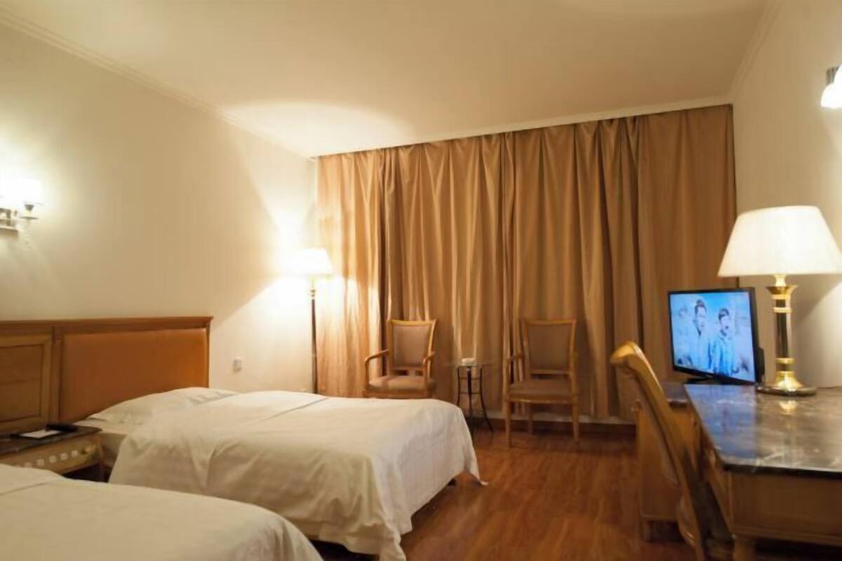 Ett hotellrum med två sängar, ett skrivbord med en lampa, en tv och en stol.