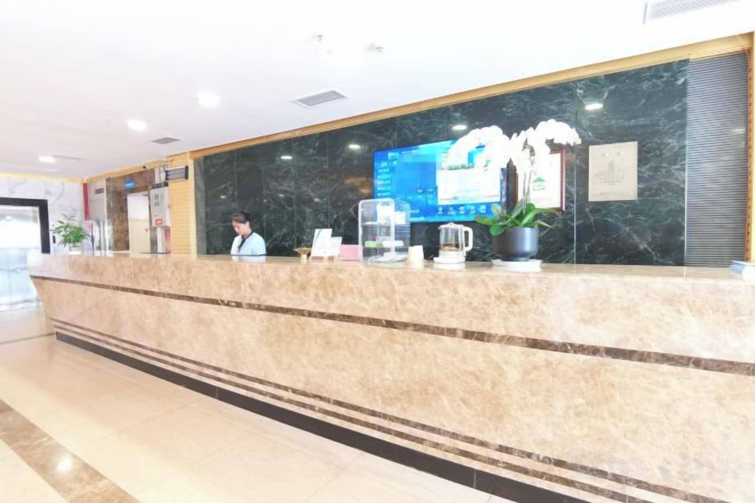 Un mostrador de recepción de hotel con encimera de mármol, una pantalla digital y un recepcionista.