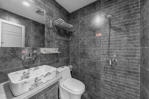 A bathroom with a toilet, a sink with a decorative basin, a shower, and a towel rack.
