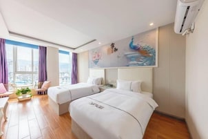 Habitación de hotel con dos camas, zona de comedor con mesa y sillas, ventana grande con cortinas y un mural en la pared.