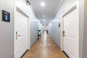 A hotel corridor with white doors, a sign on the left wall, and a plant on the right.
