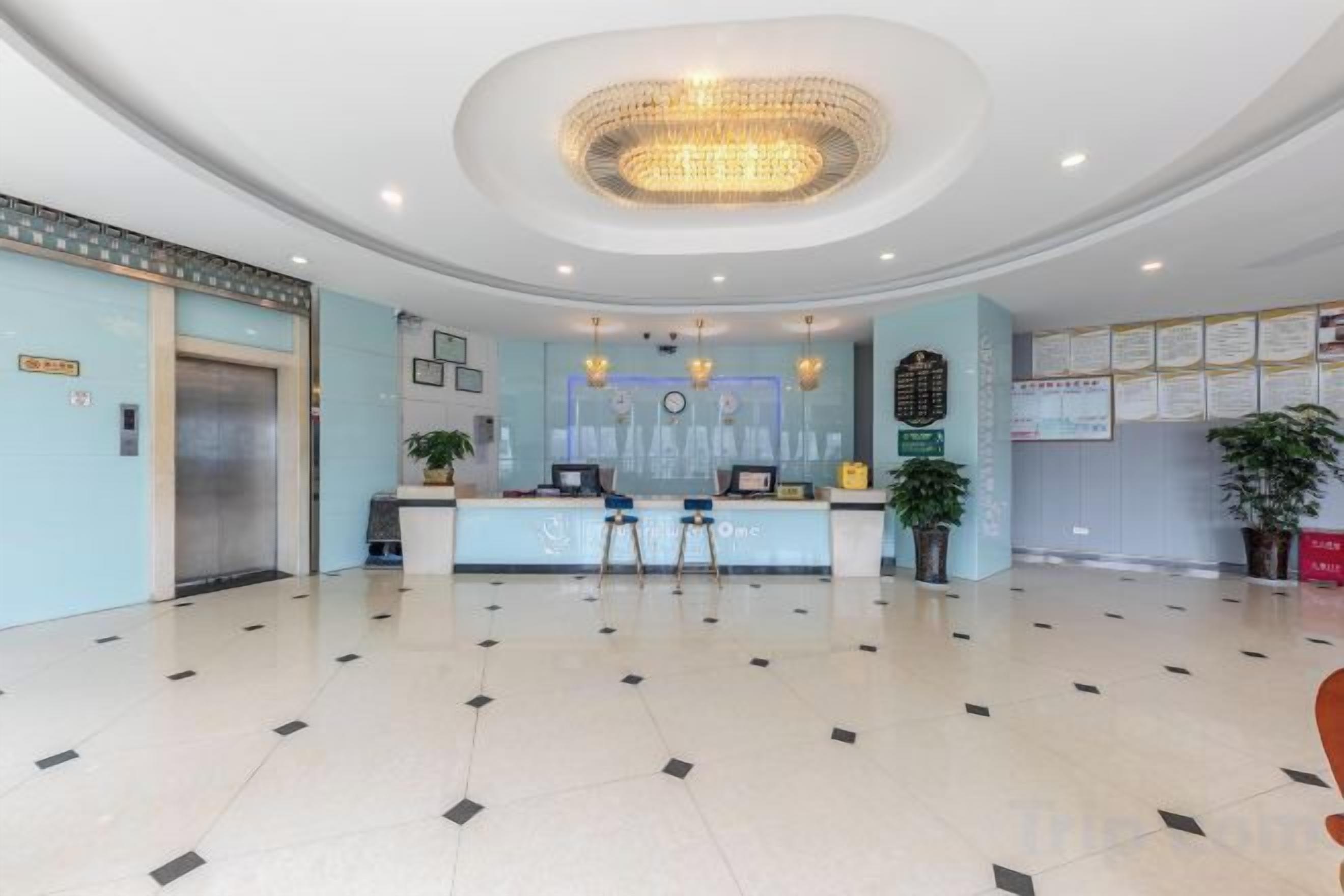 Un vestíbulo de hotel con una recepción, una araña, un reloj y un tablón de anuncios.