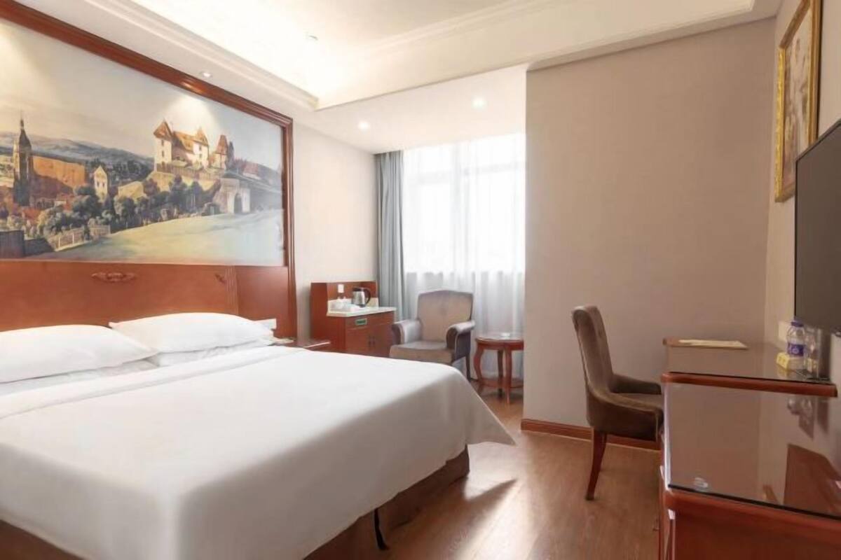 A hotel room with a large bed, a desk, a chair, a TV, and a painting on the wall.