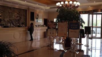 A lobby with a reception desk, a large chandelier, and a potted plant.