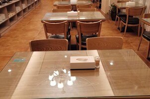 Interior de restaurante con varias mesas y sillas, una mesa de vidrio al frente y piso de madera.