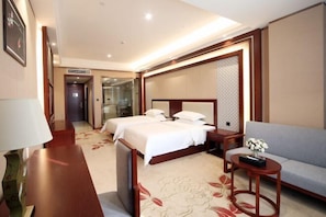 A hotel room with a large bed, a sofa, a small table, and a lamp. - Mao'nan Minzu Hotel (Huanjiang)