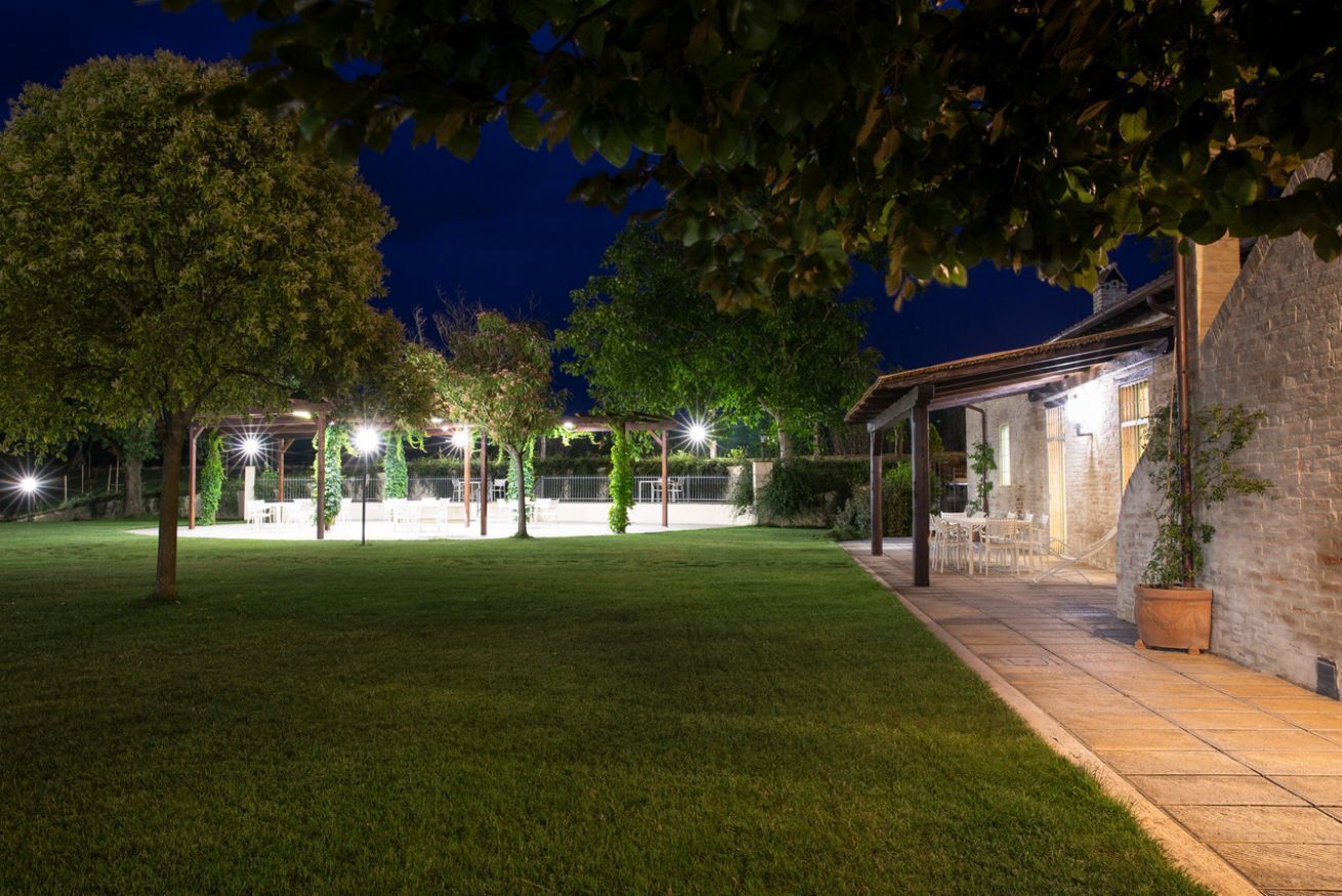 Un espacio exterior bien iluminado con una zona de estar cubierta, un edificio de piedra y un césped.