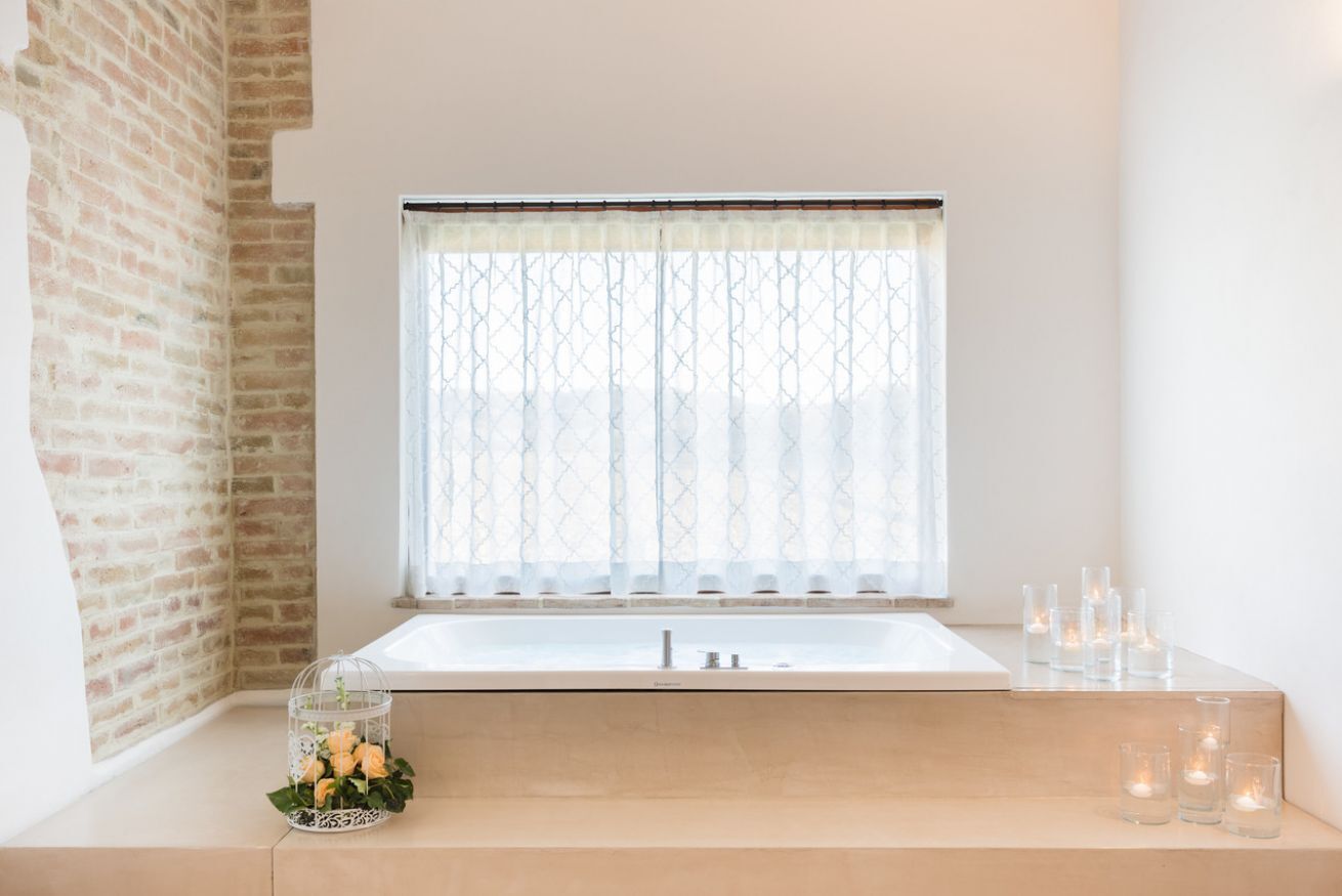 Une salle de bain moderne avec une baignoire, une fenêtre ornée de rideaux à motifs et une petite table décorée de bougies et de fleurs.