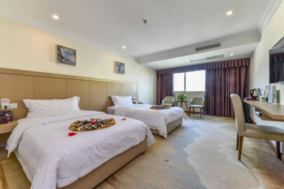 Une chambre d’hôtel avec deux lits, un bureau, une chaise et une fenêtre avec des rideaux.