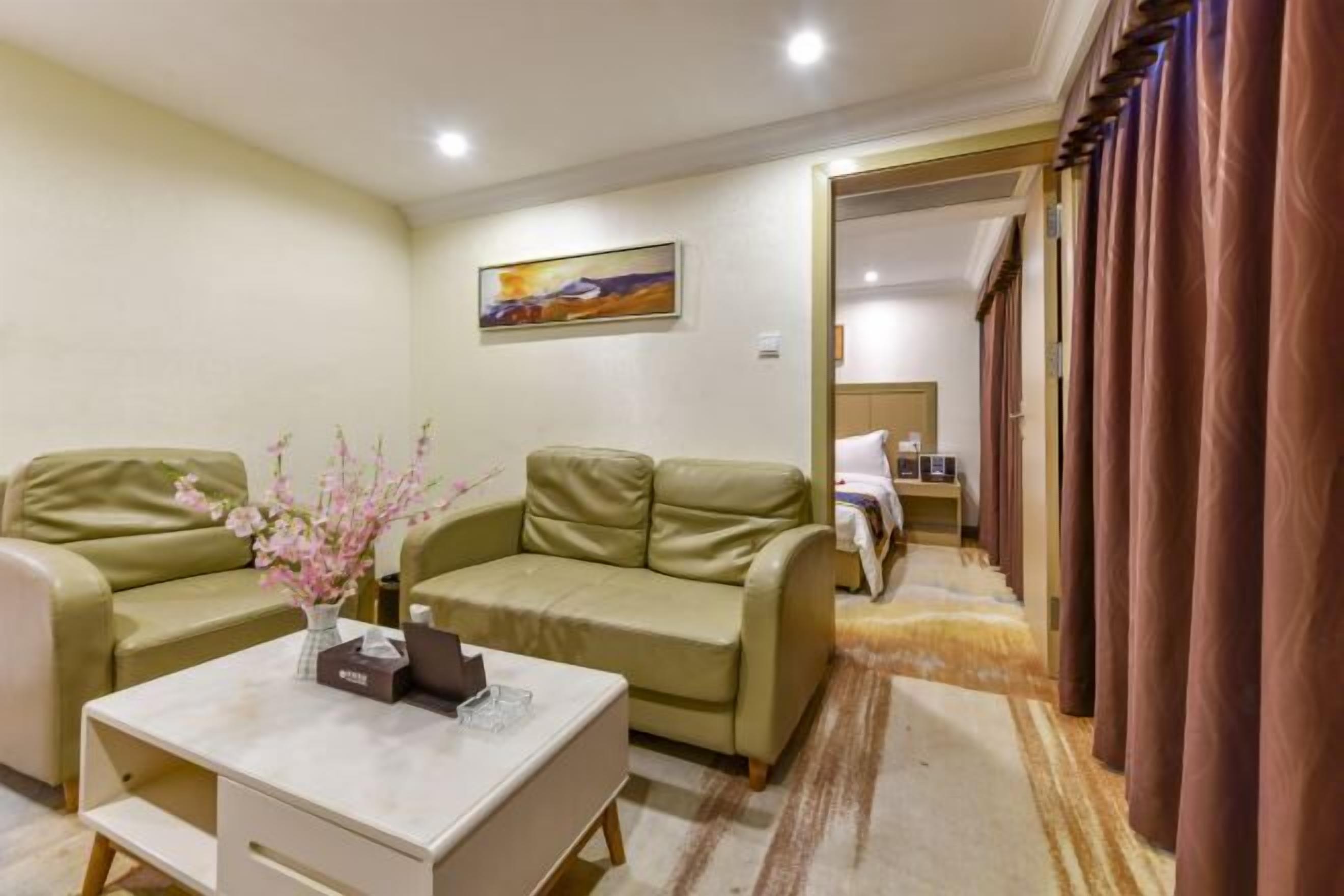 A hotel room with a beige sofa, a white coffee table with a vase of flowers, and a painting on the wall.