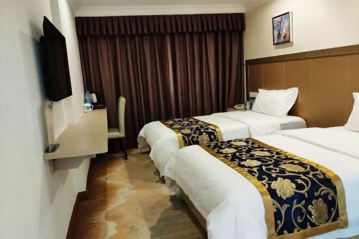Ett hotellrum med två sängar, en platt-TV, ett skrivbord med en stol och ett stort fönster med gardiner.