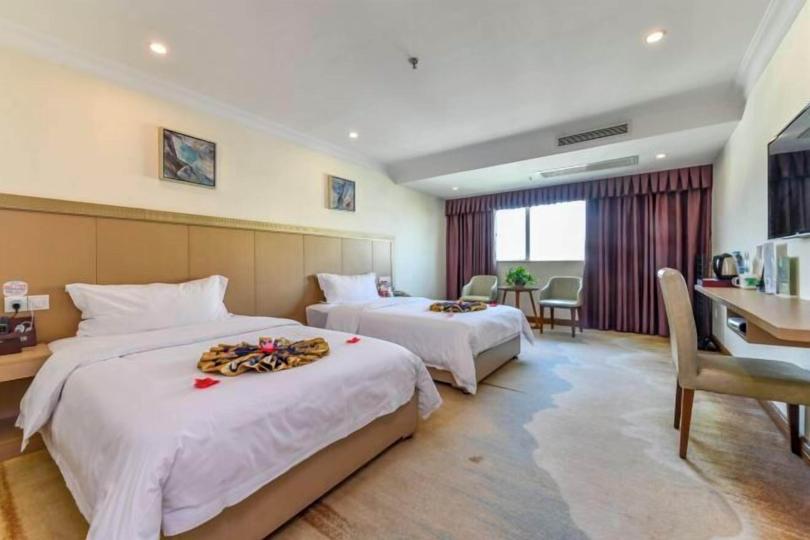 A hotel room with two beds, a desk, a chair, and a window with curtains.