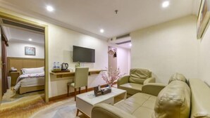 Habitación de hotel con cama, sofá, mesa de centro, televisor y escritorio con silla.