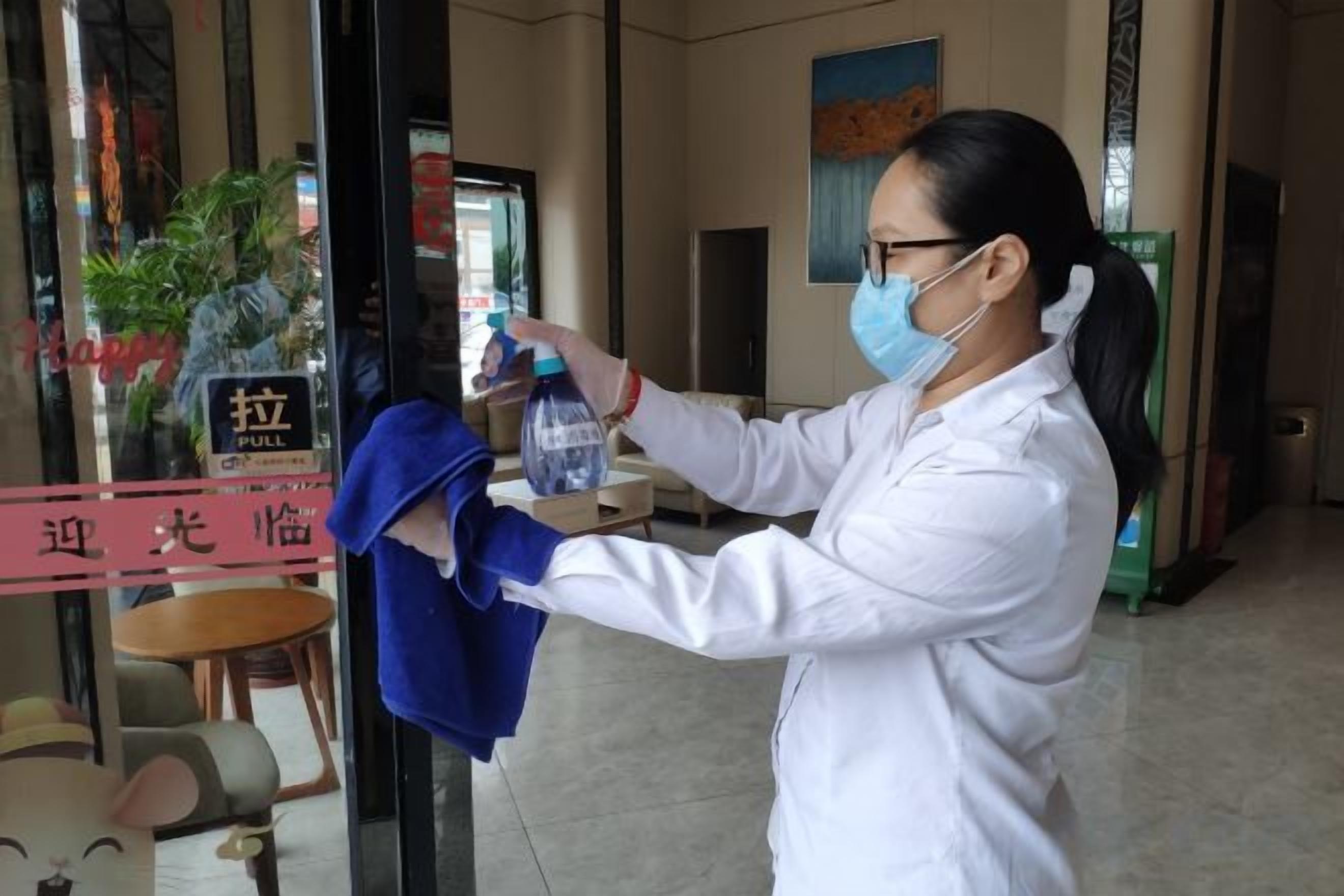 A person in a white coat holding a blue towel and a water bottle, standing in a room with a glass door and a sign that says 'pull.'