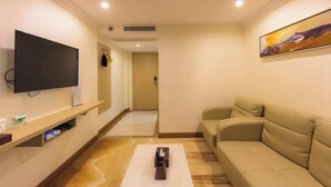 Habitación de hotel con televisor de pantalla plana en la pared, un sofá color beige y un cuadro en la pared.