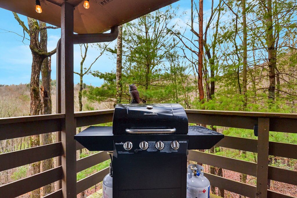 A barbecue grill on an outdoor deck with a view of trees and a clear sky.