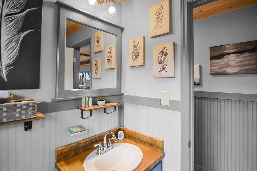 A bathroom with a wooden vanity, a large mirror, and multiple framed leaf artworks on the wall.