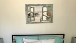 Un dormitorio con cama, dos almohadas, una mesita de noche y un espejo montado en la pared.