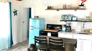 Una cocina con un refrigerador azul, un microondas y una estufa. Hay una mesa de comedor con sillas y una lámpara colgante.