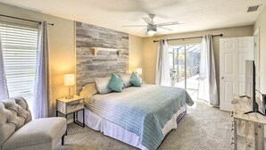 Un dormitorio con una cama grande, un ventilador de techo, una mesita de noche con lámpara, una silla y una pared decorativa de madera.