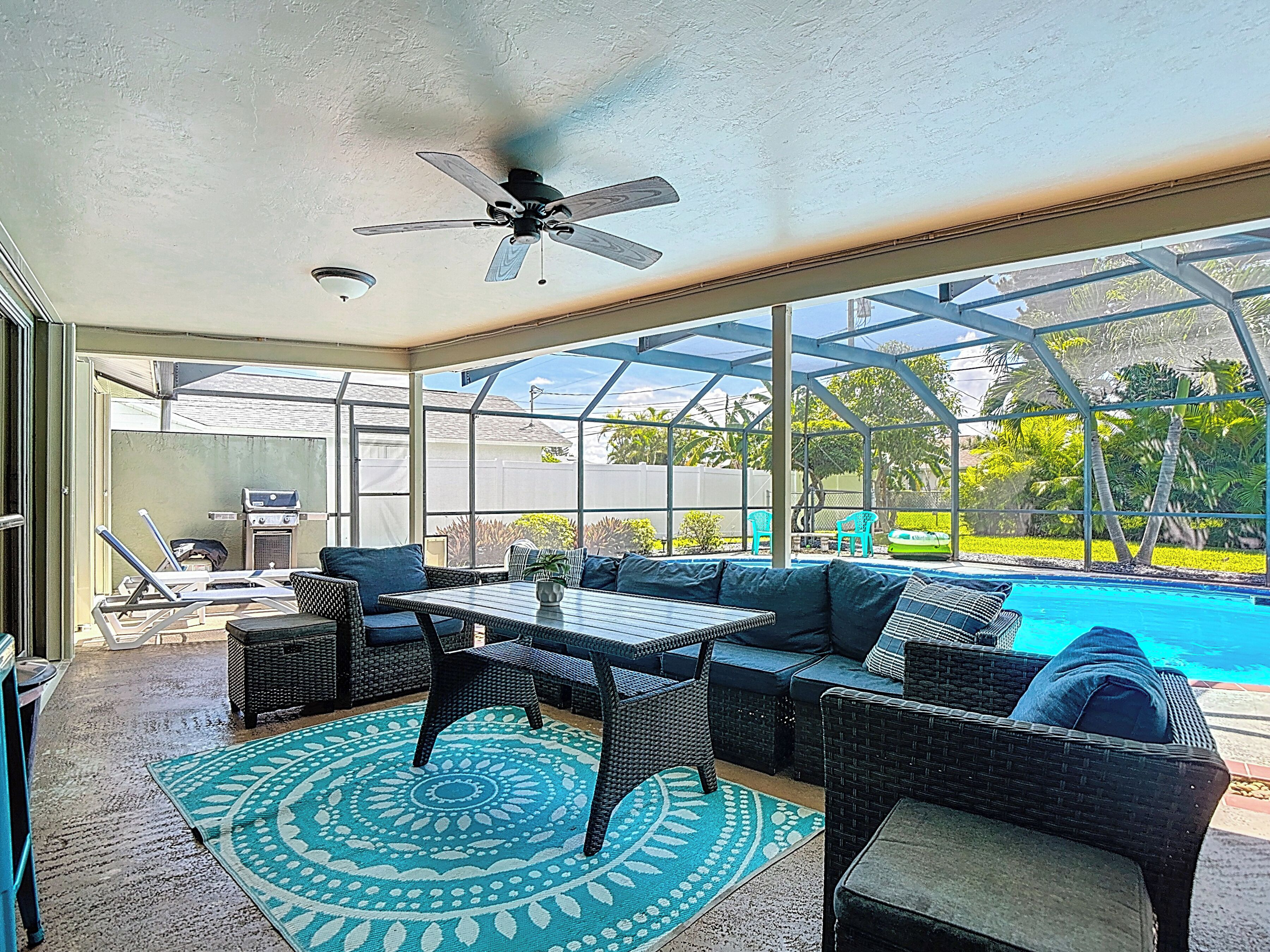 Ein überdachter Außenbereich mit Pool, Deckenventilator und Blick auf den Garten.