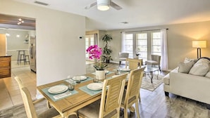 Un comedor con una mesa de madera preparada para cuatro personas, un ventilador de techo y vista al salón con un sofá y una lámpara.