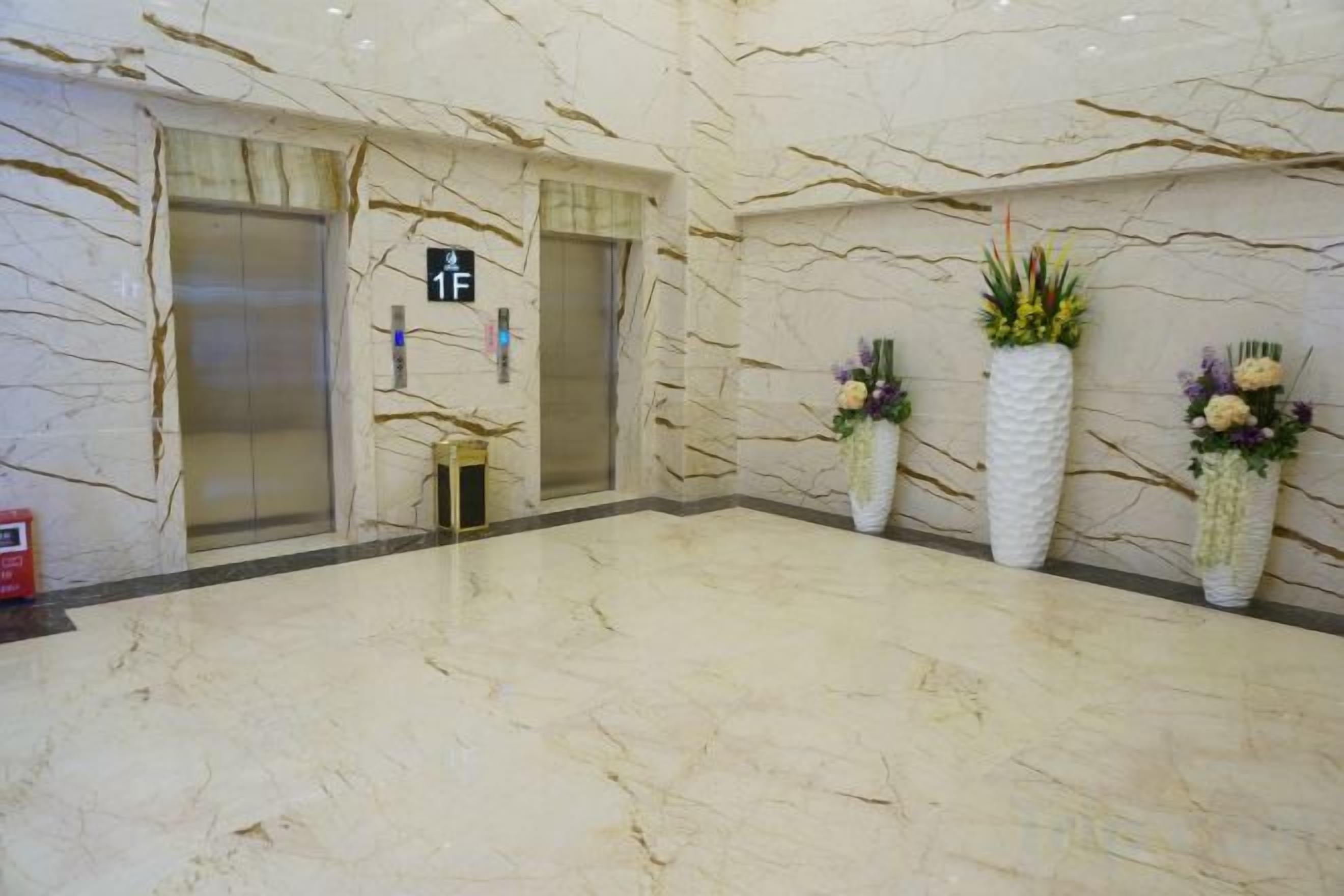 A marble-floored lobby with two elevators, a fire extinguisher, and three potted plants.