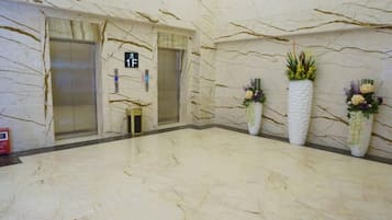 A marble-floored lobby with two elevators, a fire extinguisher, and three potted plants.